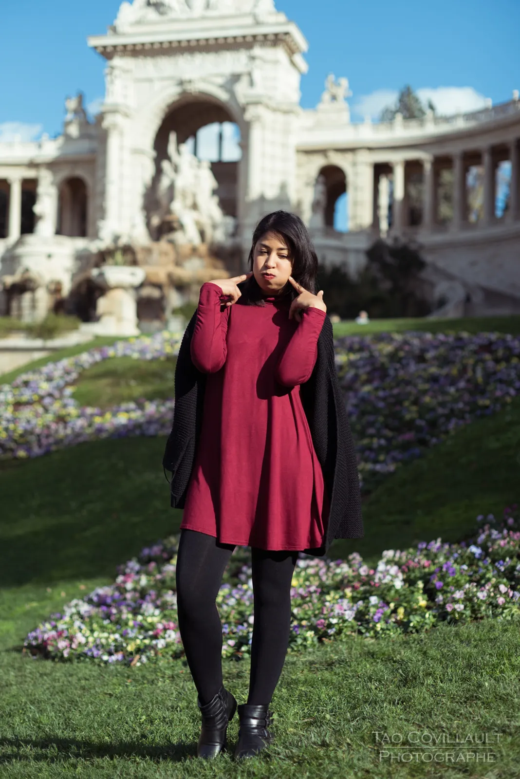 Woman in a burgundy dress standing on a lawn in front of an ornate building.