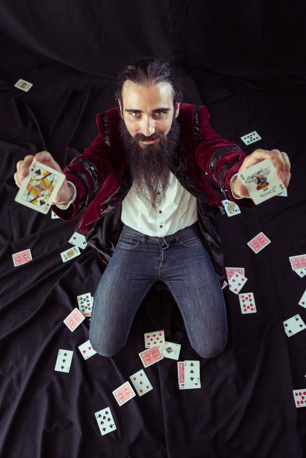 Bearded performer posing amid floating playing cards.
