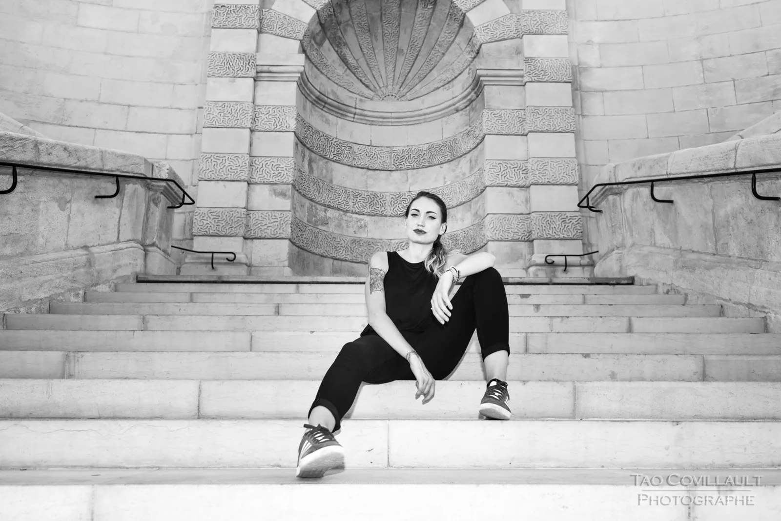 Black-and-white photograph: woman in black clothing posing on pale stone steps.