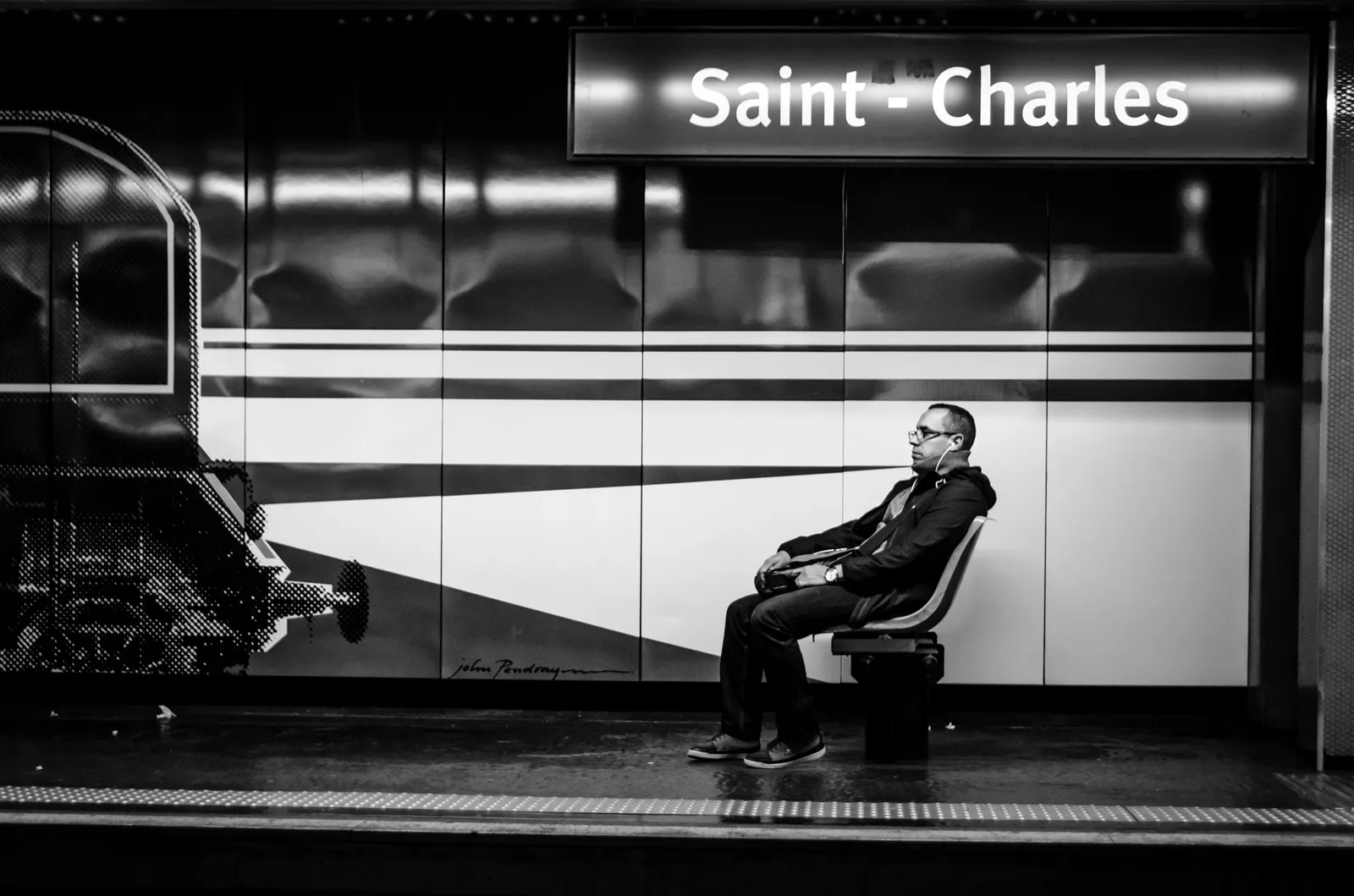 Seated passenger beneath a Saint-Charles station sign in black and white