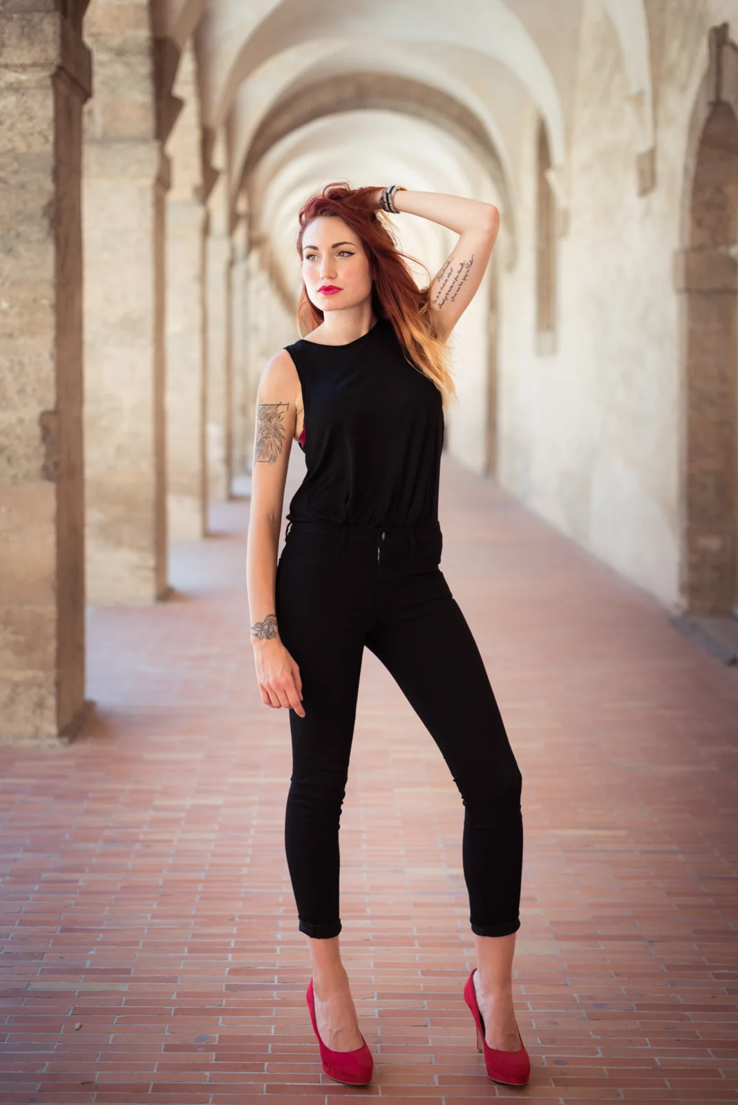 Woman in black clothing posing in a stone arcade.