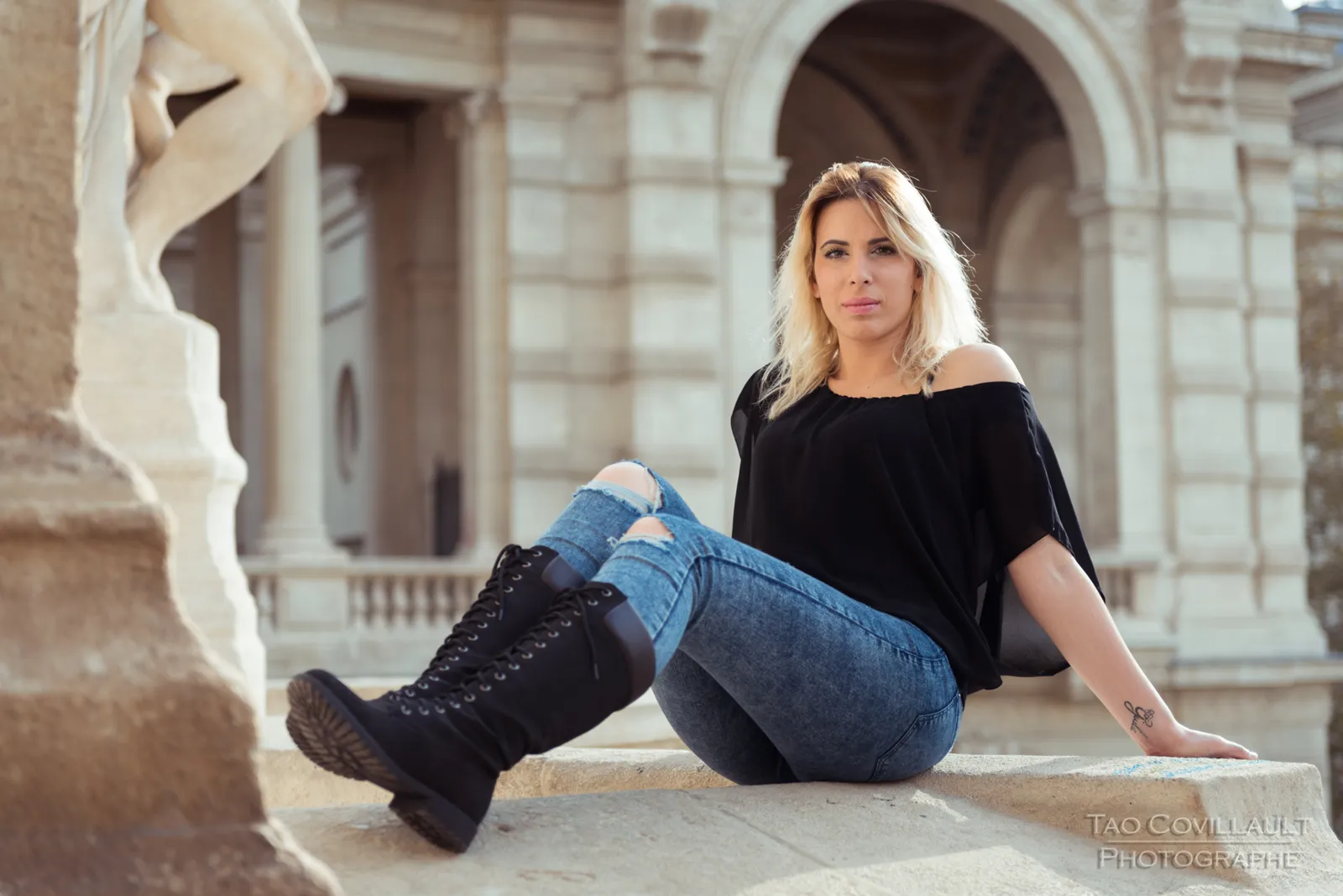 Woman in a black top and jeans seated on a stone balustrade.