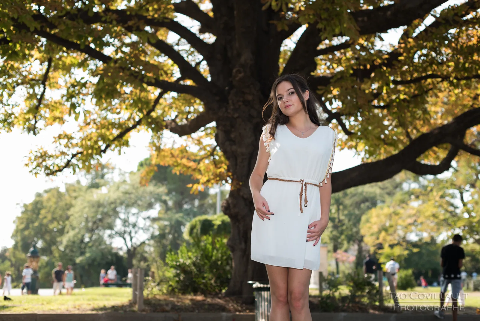 Woman in a white dress standing beneath a broad leafy tree.
