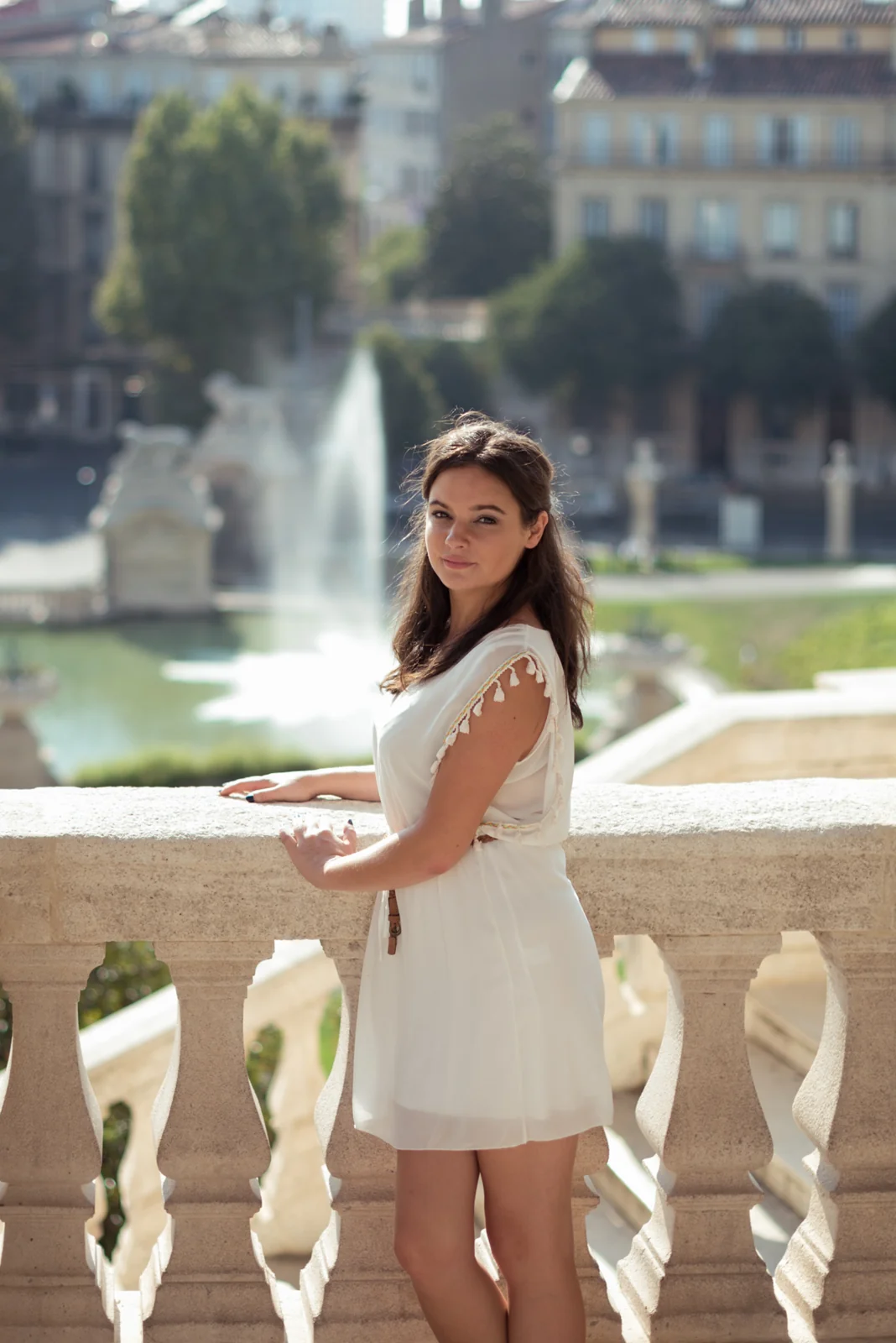 Woman in a white dress posing on stone steps and beside a balustrade.