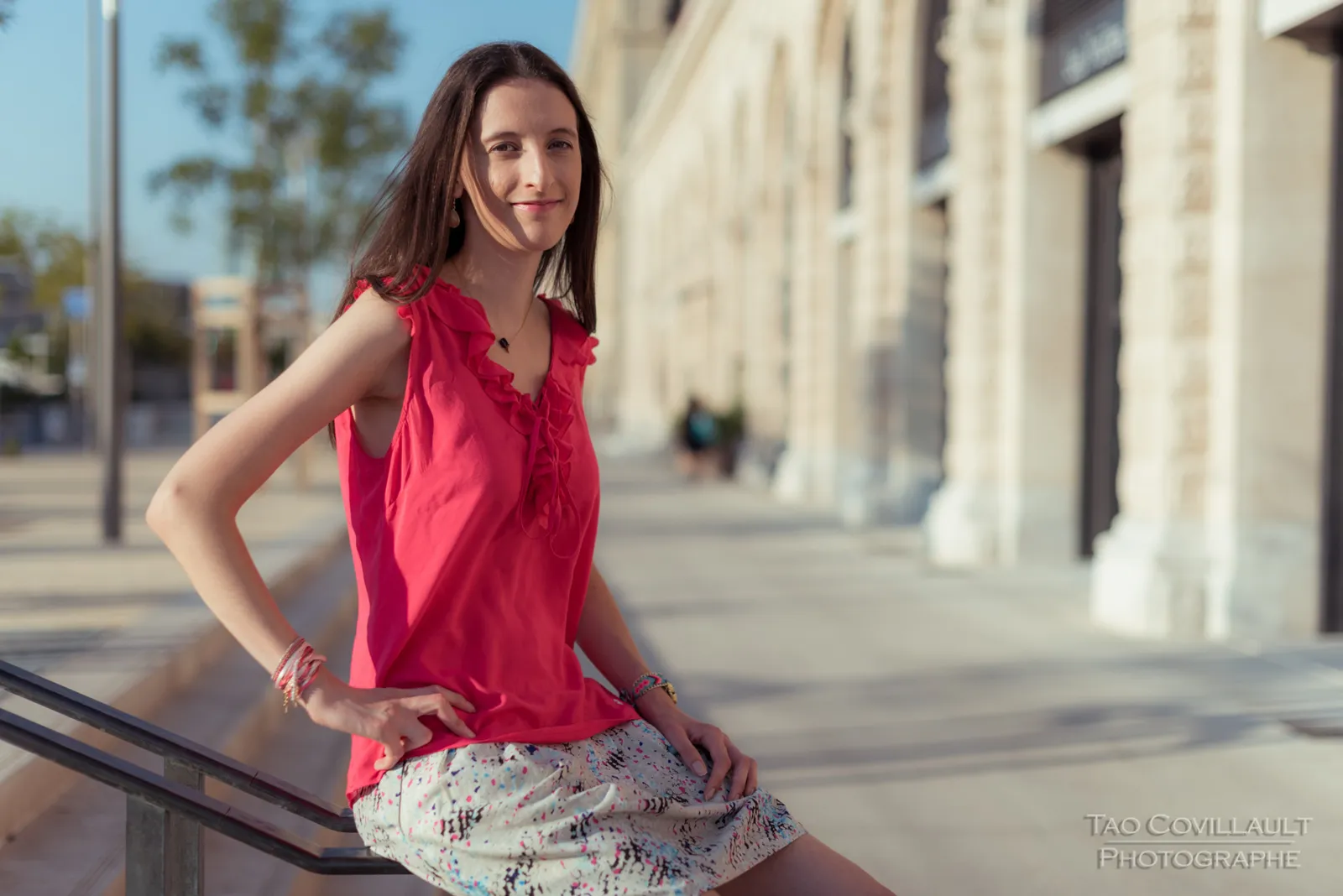 Woman in a bright pink top and patterned skirt posing beside stone steps and walls.