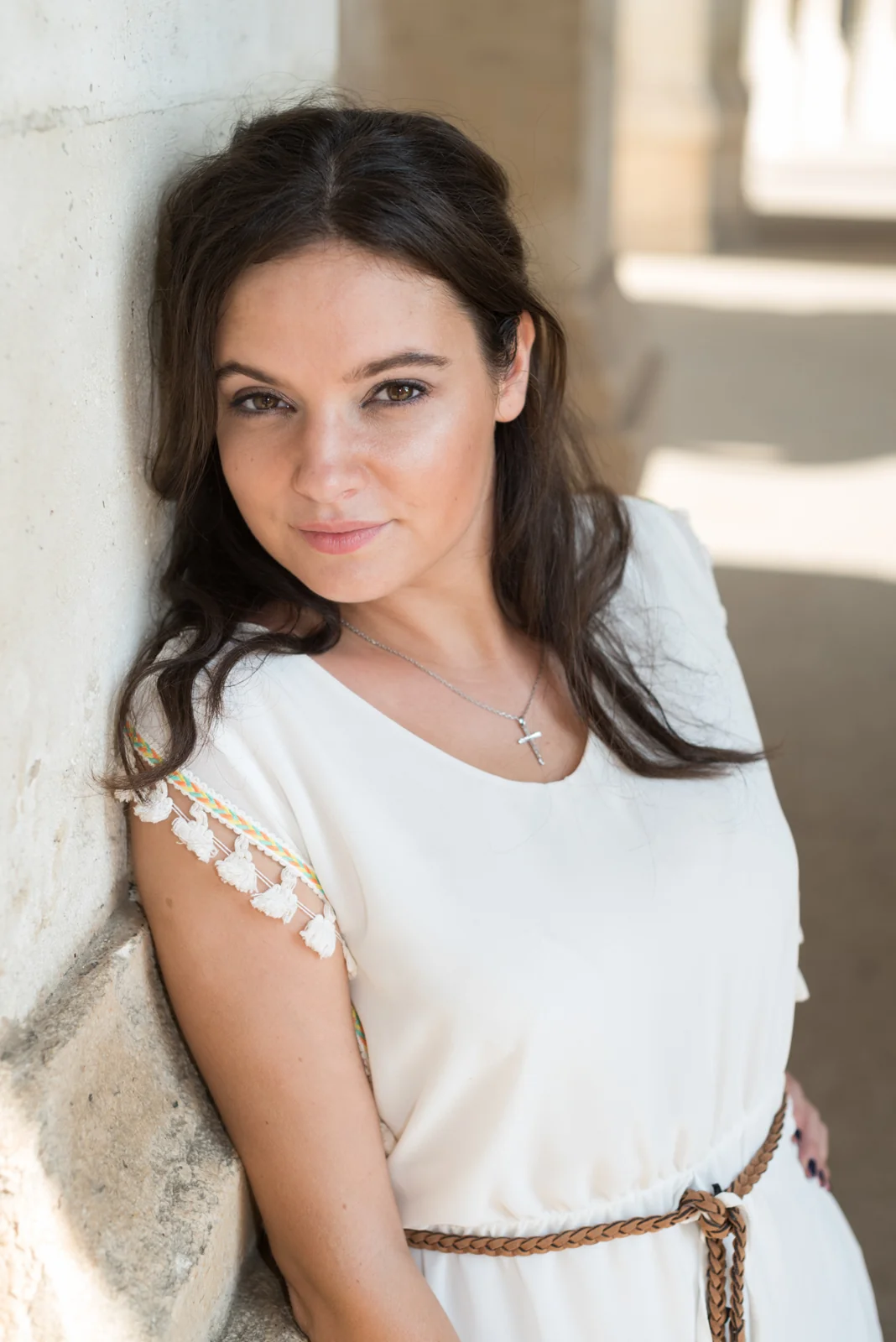 Portrait of a woman in a white dress beside a stone column.