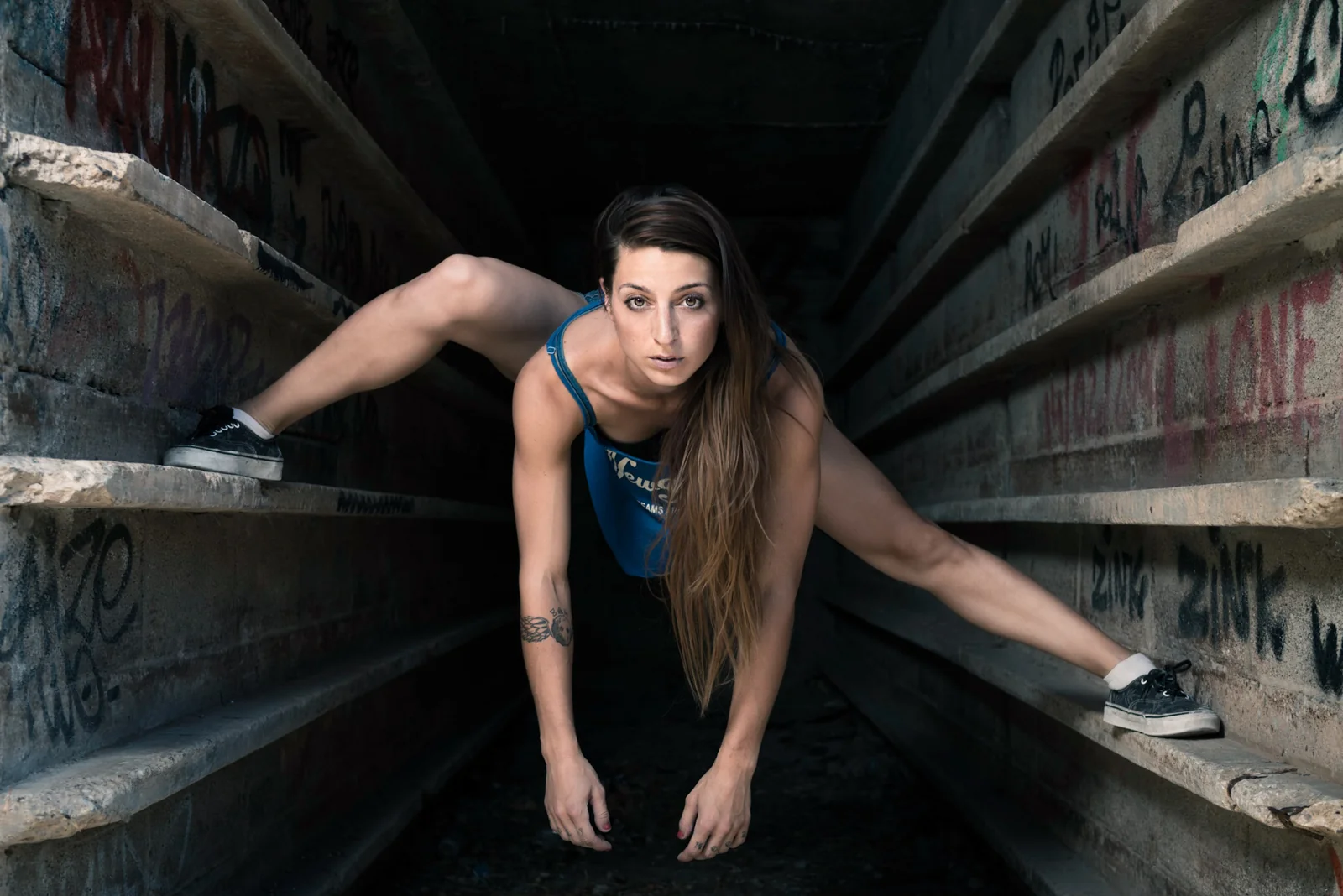 Dancer crouching between weathered industrial beams.