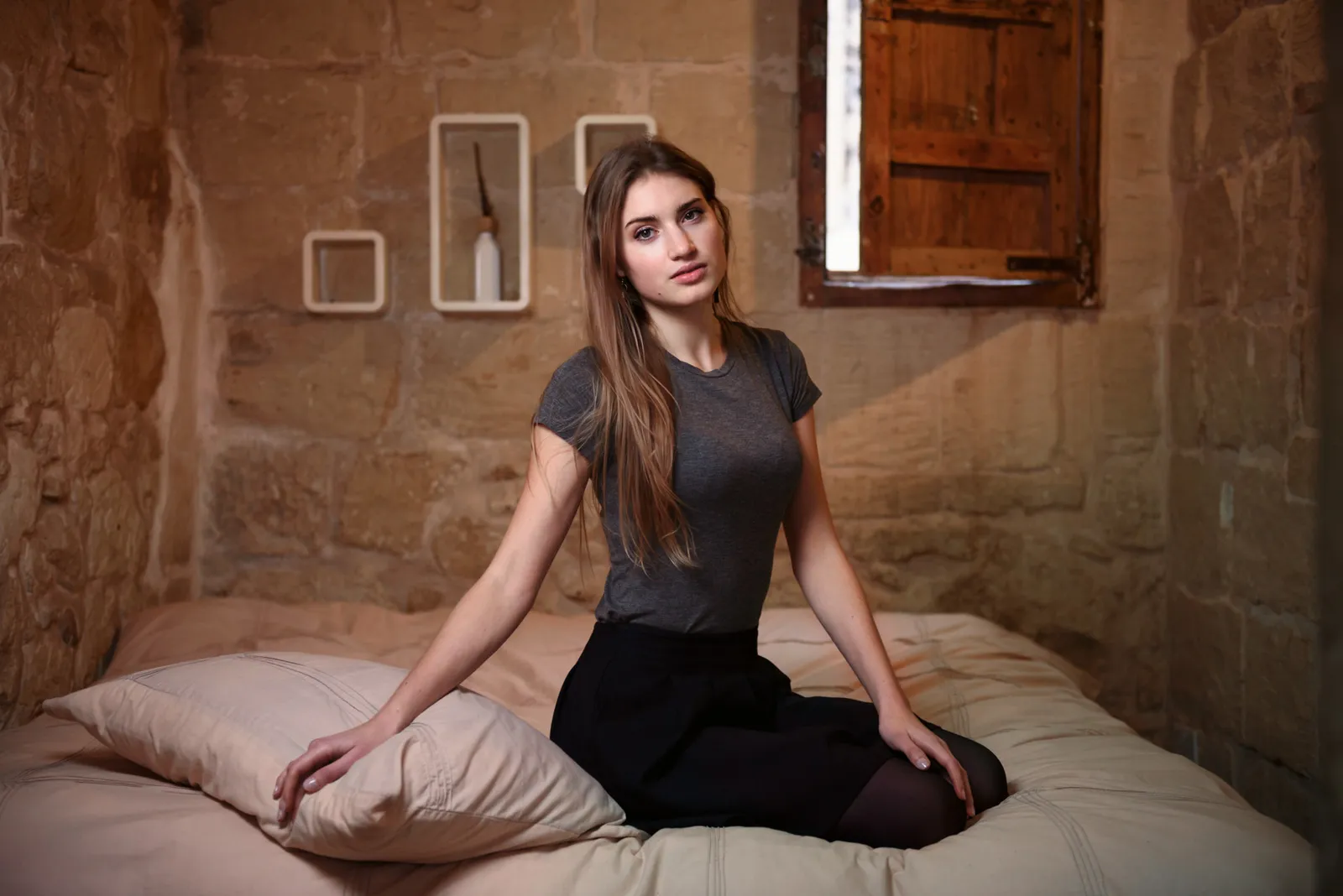 Woman dressed in black seated on a bed.