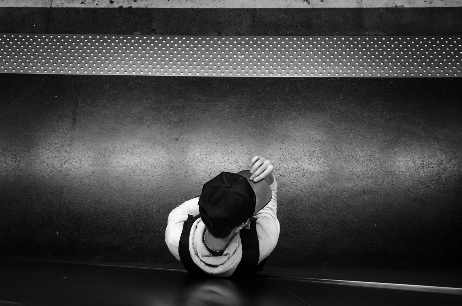 Overhead view of a person in a hat beside a dark station wall