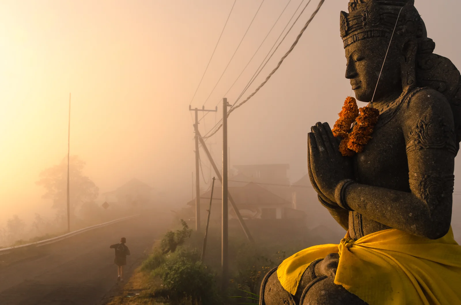 Stone statue beside a misty road at sunrise
