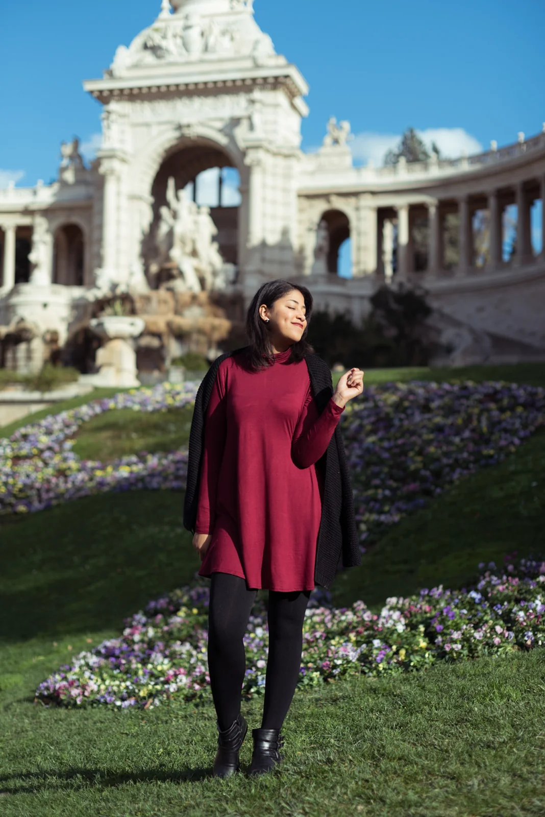 Woman in a burgundy dress standing on a lawn in front of an ornate building.