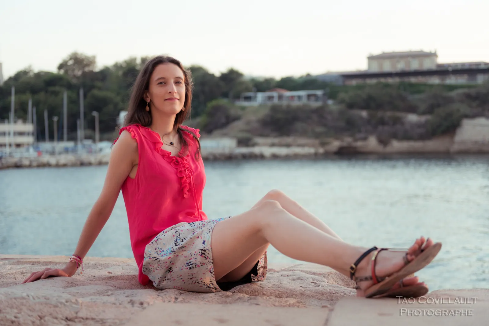 Woman in a pink top seated beside the waterfront.