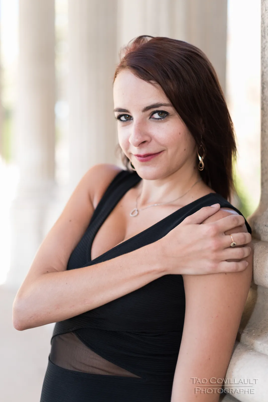 Woman in a black dress posing near pale stone columns.