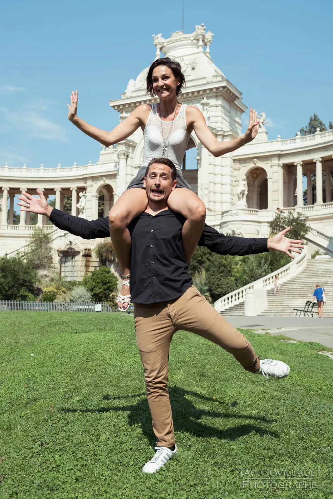 Couple posing playfully on a lawn in front of an ornate building.