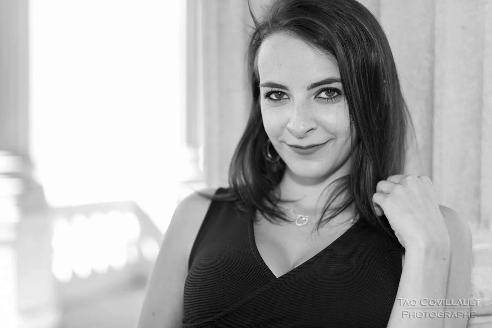 Black-and-white photograph: woman in a black dress posing near pale stone columns.