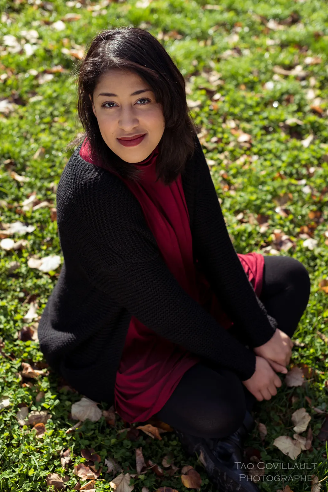 Woman in a burgundy dress and dark coat sitting among trees.