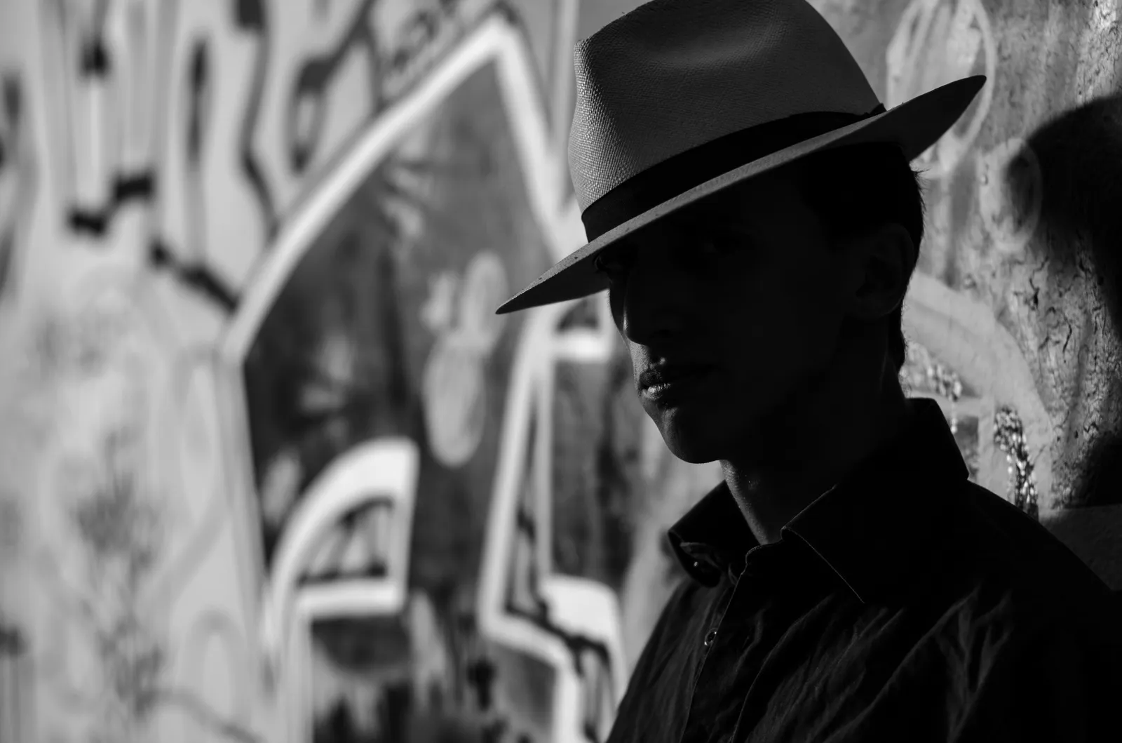 Shadowed portrait of a person in a hat against graffiti