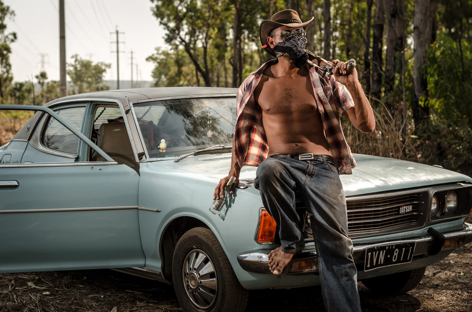 Person in a hat and open shirt standing beside a vintage car