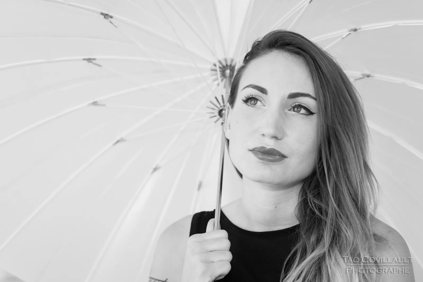 Black-and-white photograph: woman in black clothing holding a white parasol.