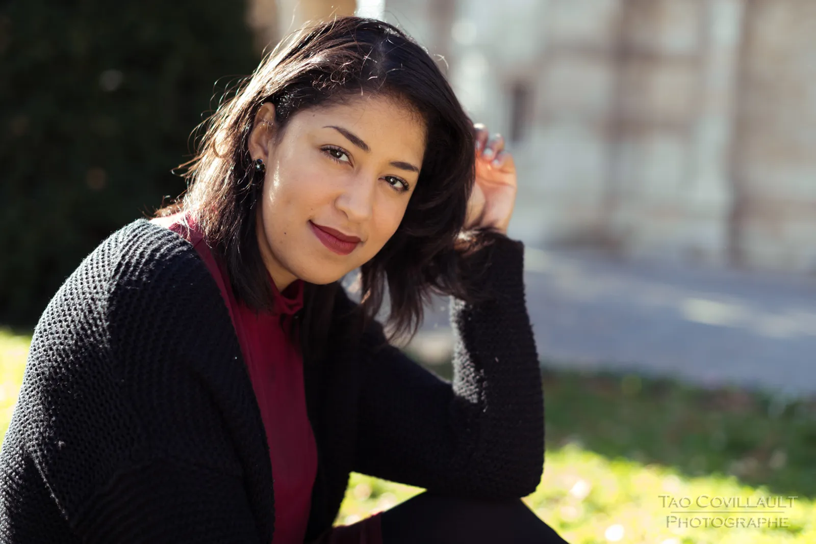 Woman in a burgundy dress and dark coat sitting among trees.