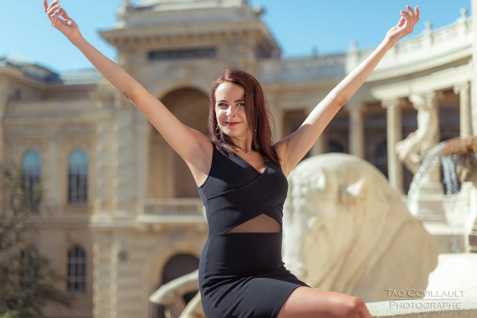 Woman raising both arms beside a carved stone sculpture.