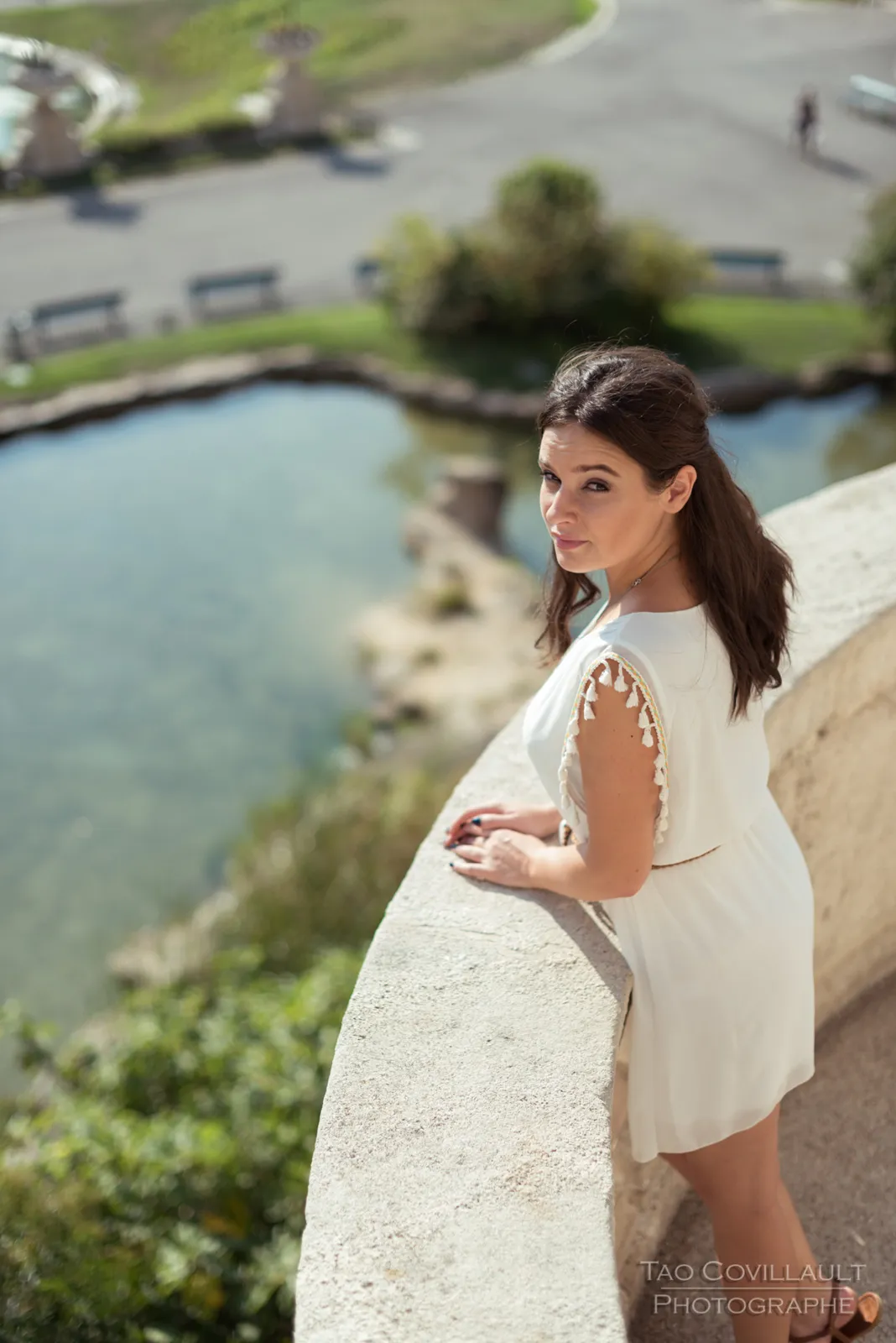Woman in a white dress posing on stone steps and beside a balustrade.