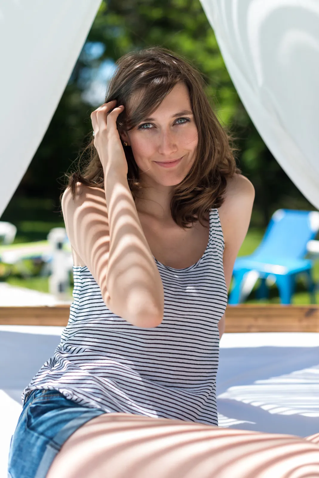 Woman in a striped top seated beneath white poolside curtains.
