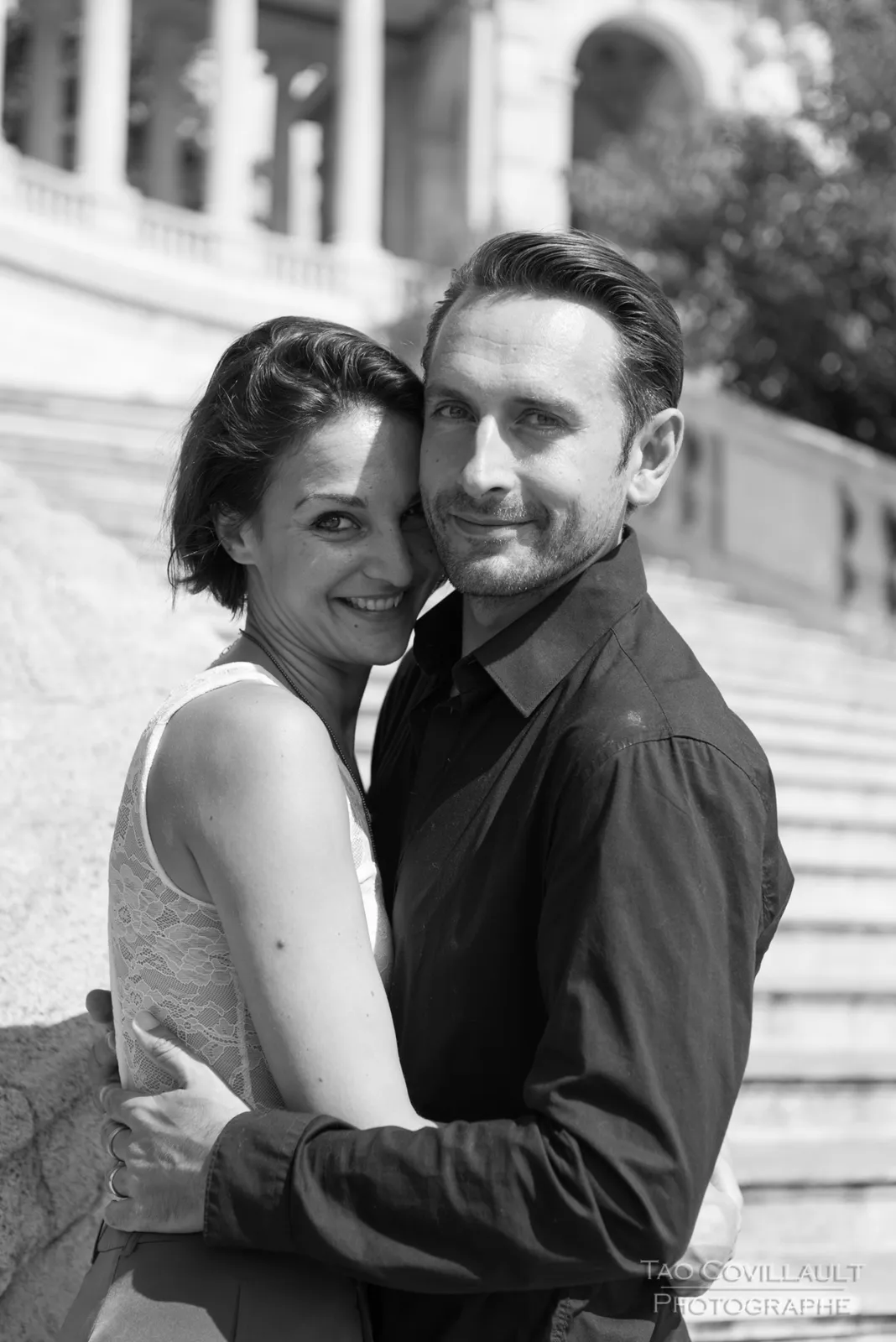 Black-and-white photograph: couple embracing beside a stone balustrade.