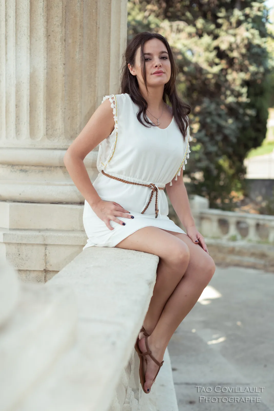 Woman in a white dress posing among pale stone columns.