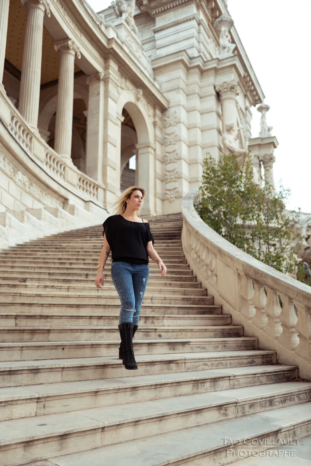 Woman in a black top and jeans posing on a stone terrace and steps.