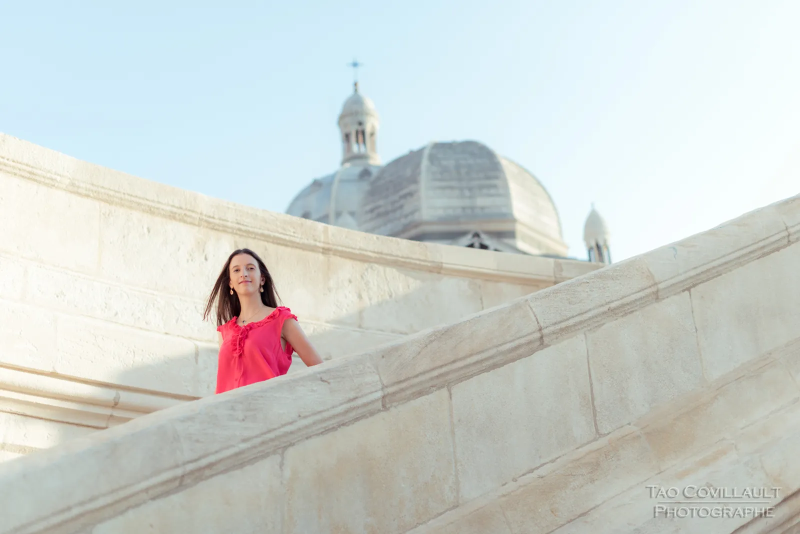 Woman in a bright pink top standing behind a curved stone wall.