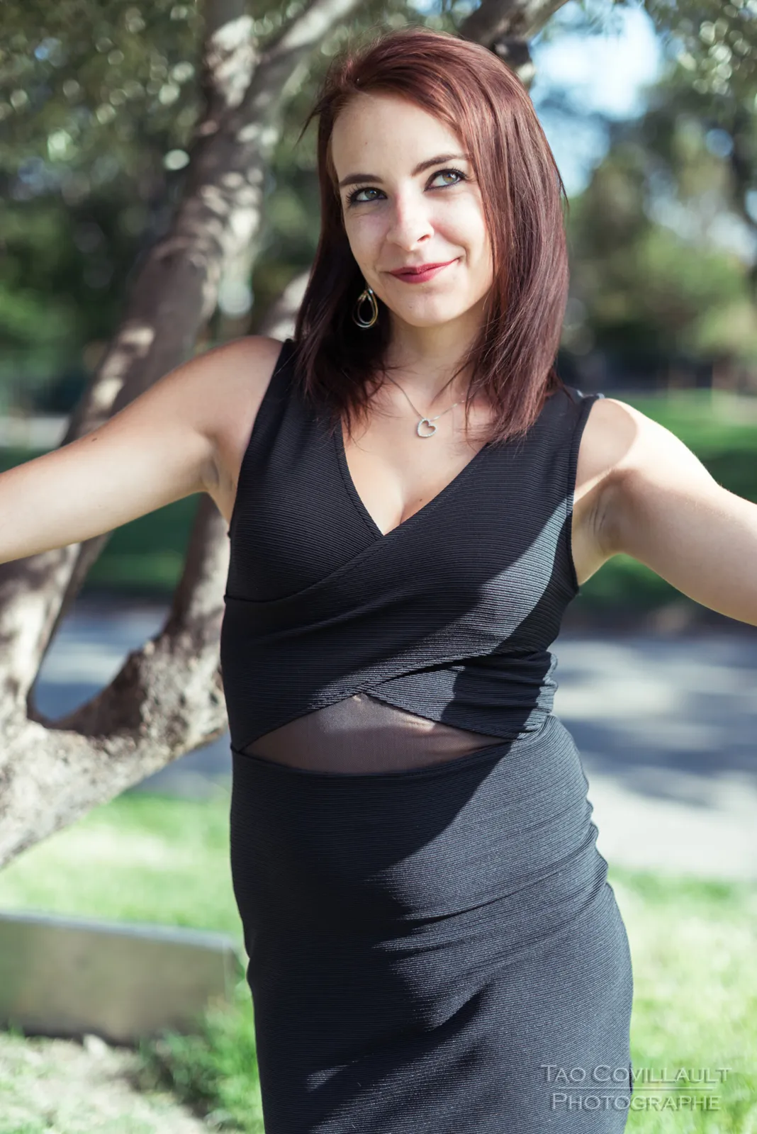 Woman in a black dress posing among trees.
