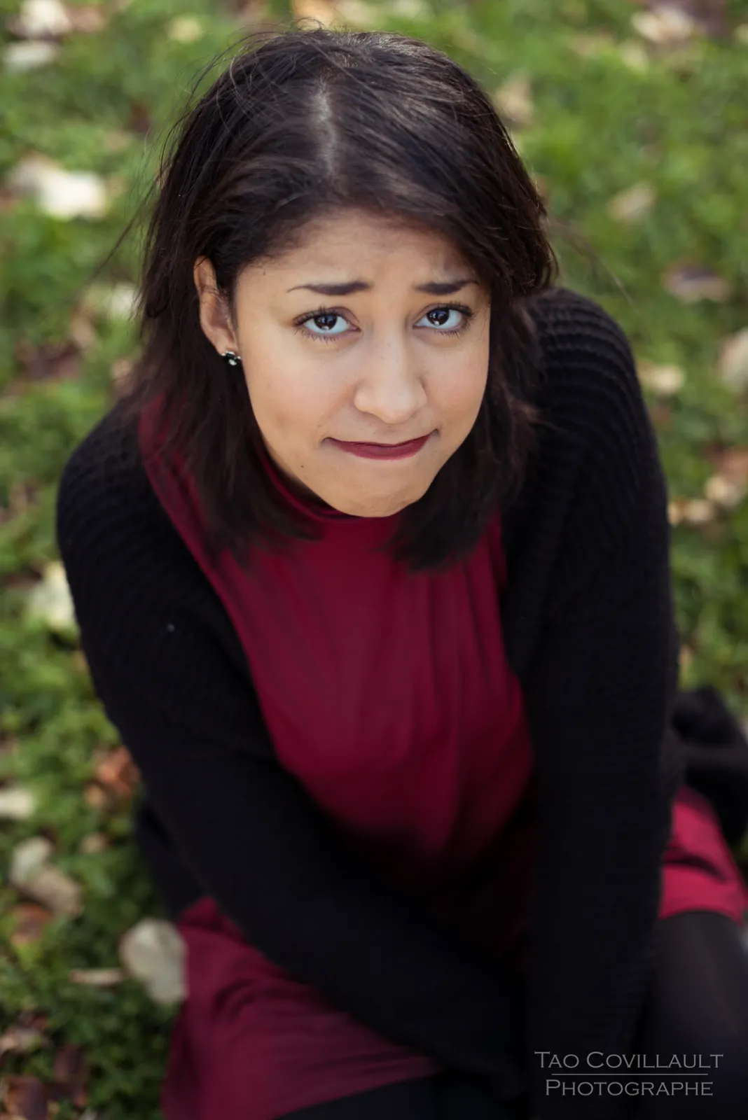 Woman in a burgundy dress and dark coat sitting among trees.