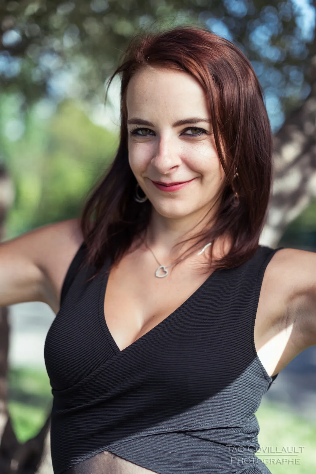 Woman in a black dress posing among trees.