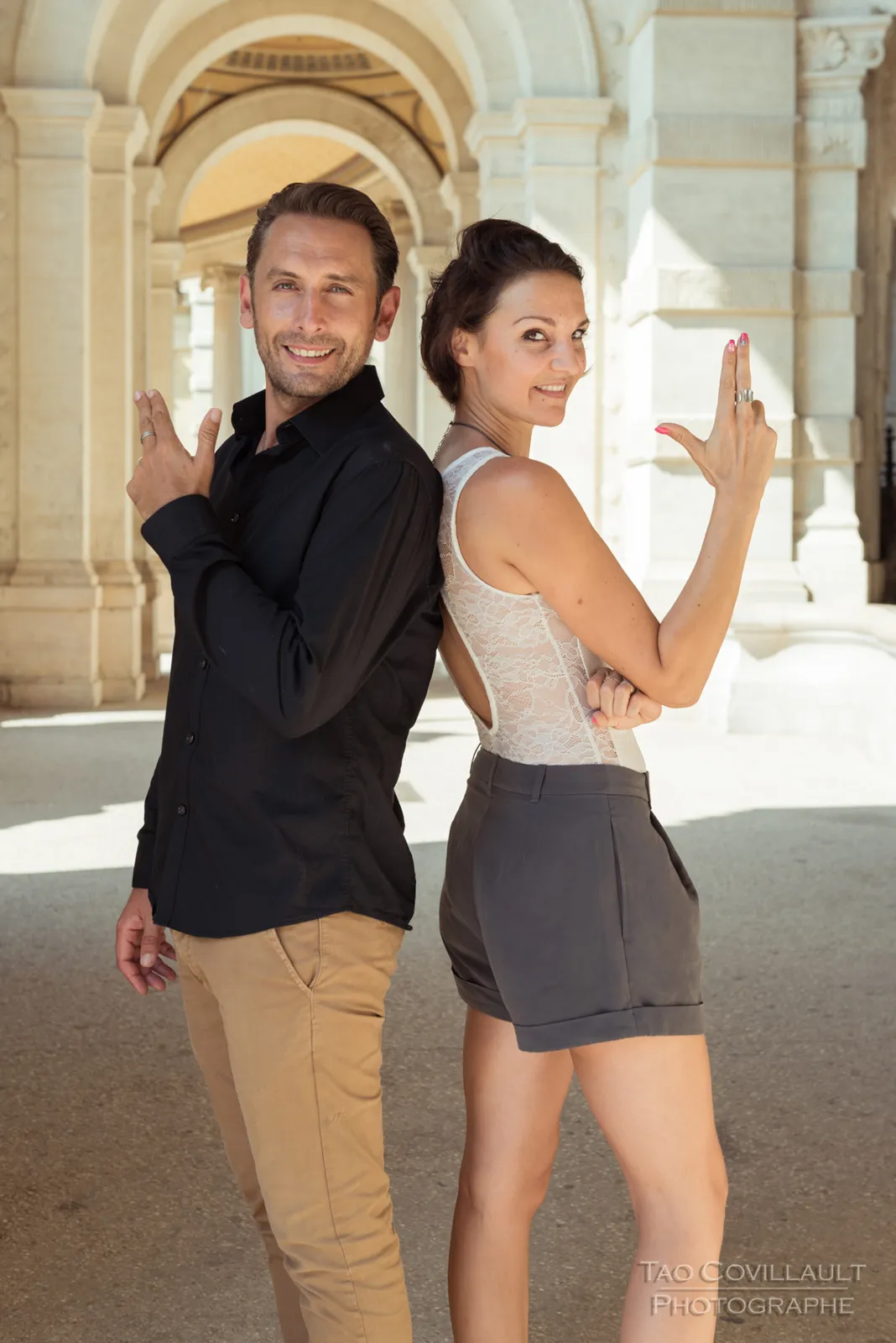 Couple posing back to back in a stone arcade.
