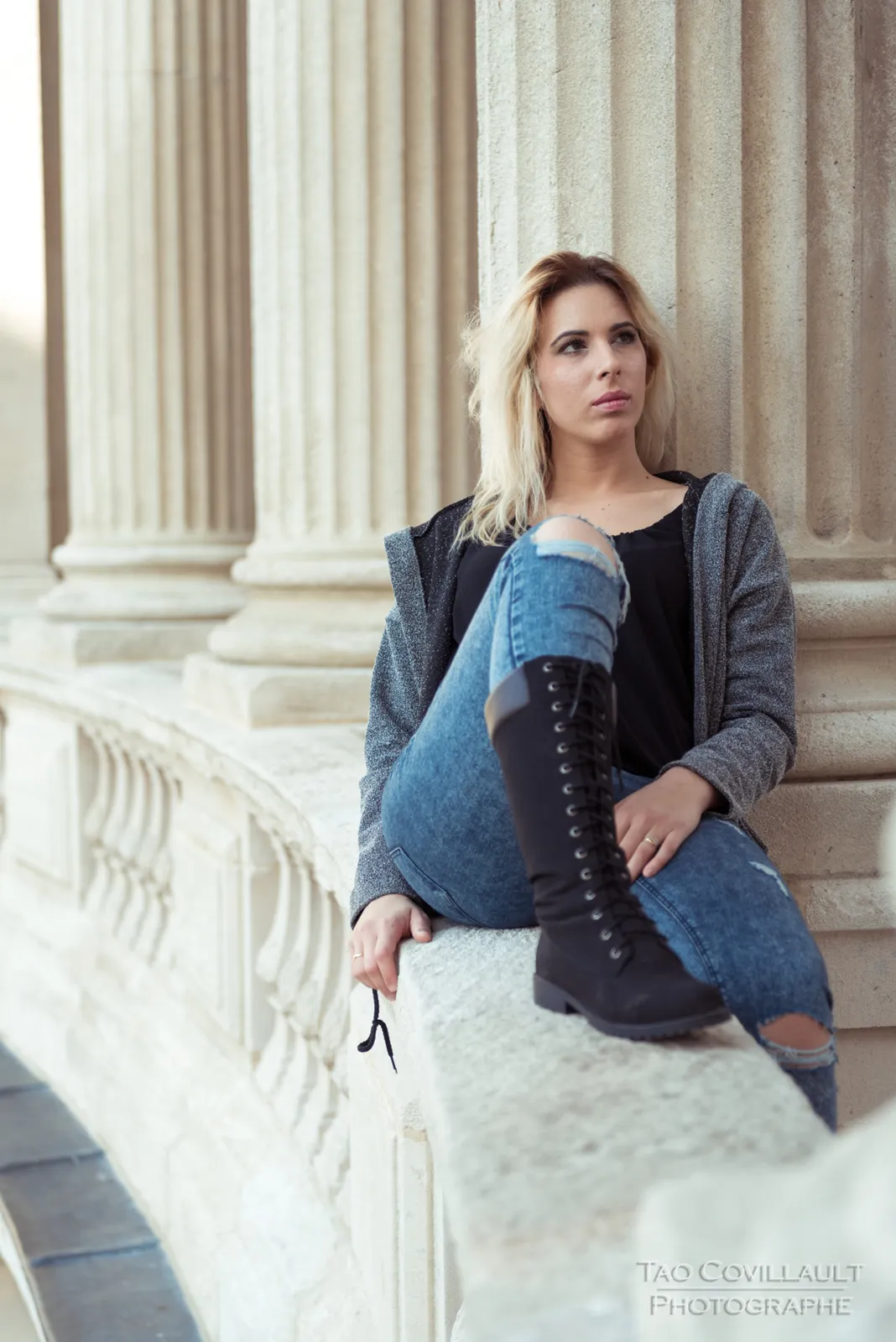 Woman in jeans and a dark jacket posing beside stone columns.