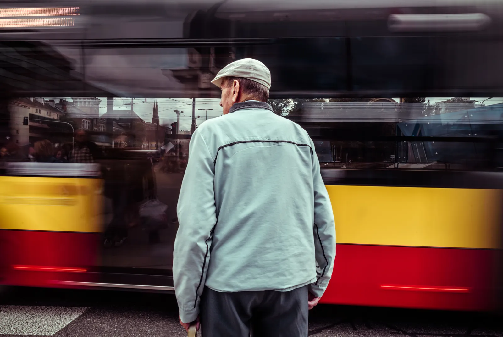 Person in a pale jacket beside a passing red and yellow tram