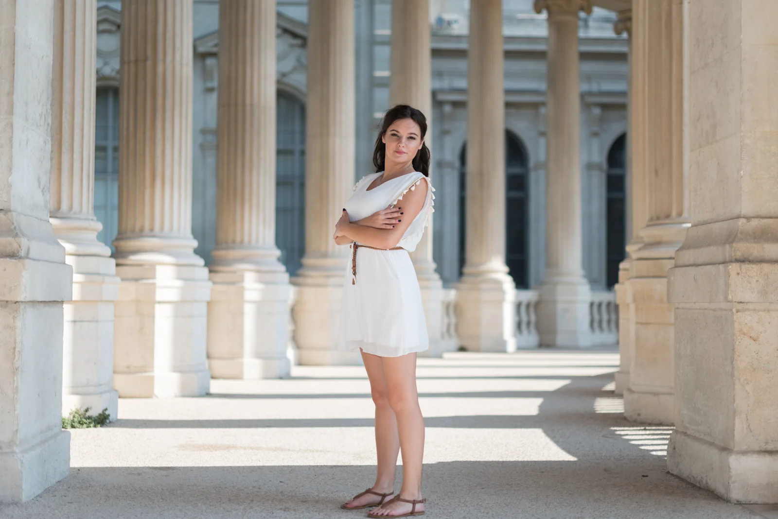Woman in a white dress posing among pale stone columns.