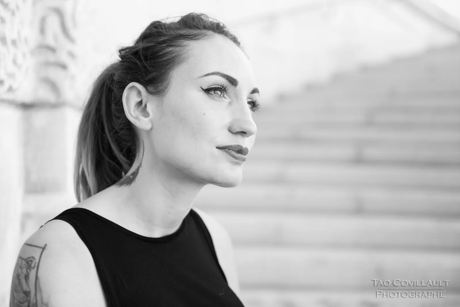 Black-and-white photograph: woman in black clothing posing on pale stone steps.