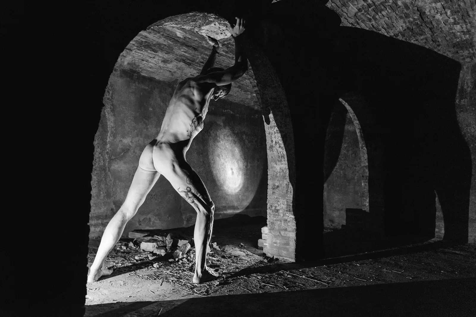 Standing figure casting a long shadow beneath stone arches