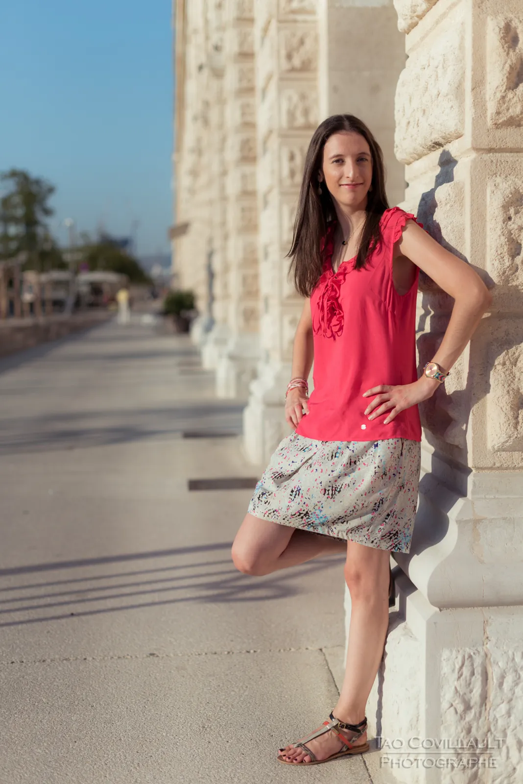Woman in a bright pink top and patterned skirt posing beside stone steps and walls.