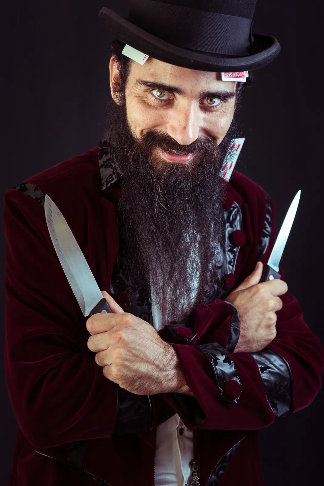 Bearded performer in a top hat holding knives.