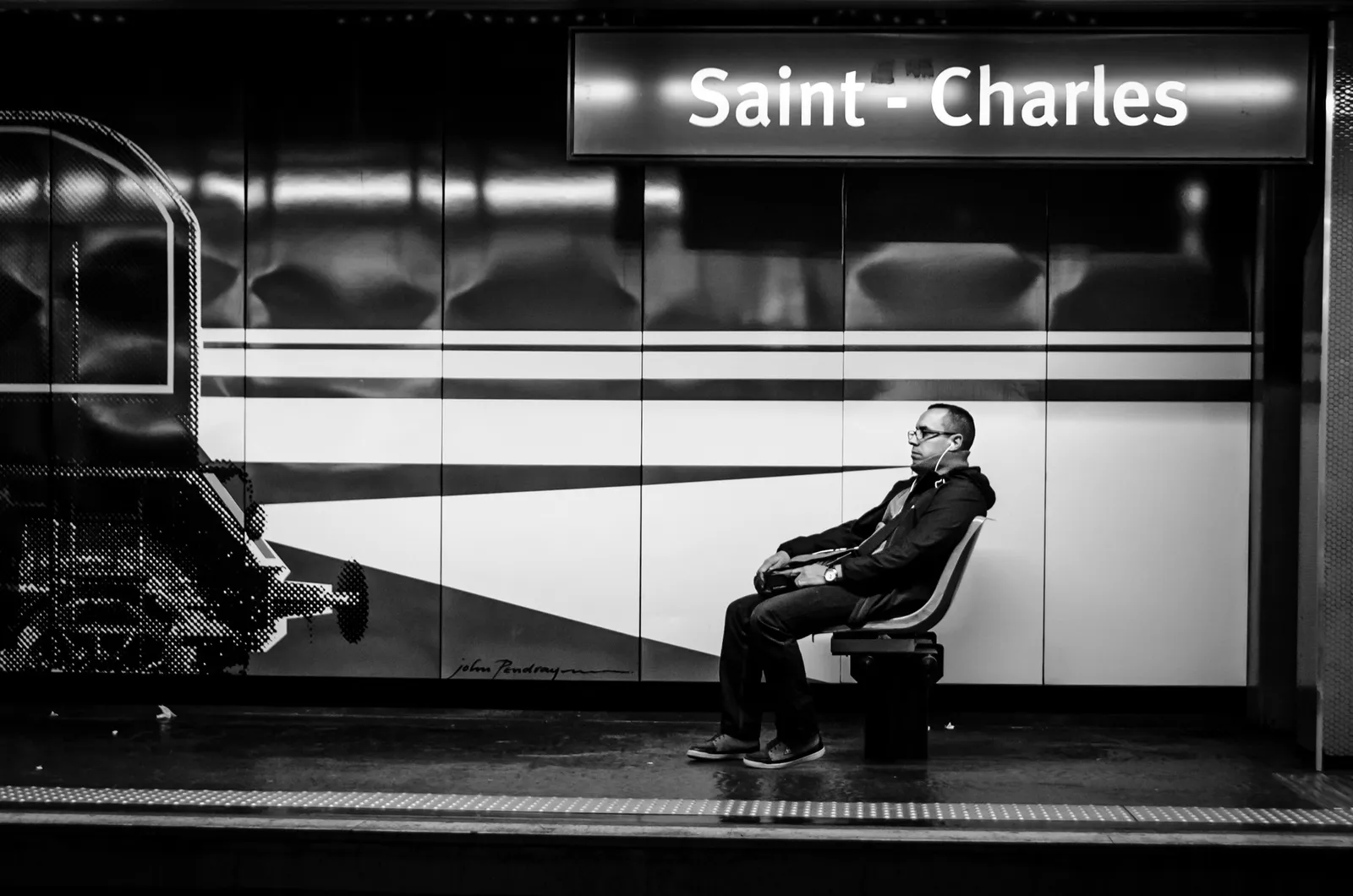 Seated passenger beneath a Saint-Charles station sign in black and white
