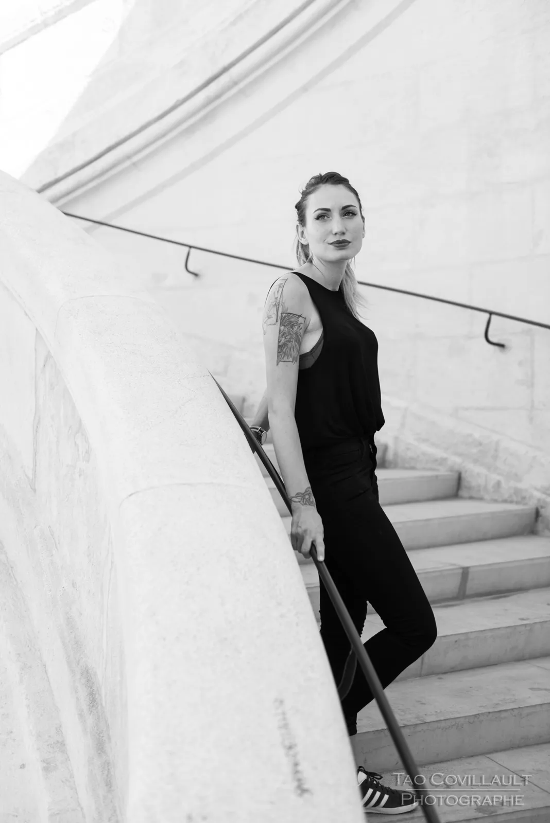 Black-and-white photograph: woman in black clothing posing on pale stone steps.