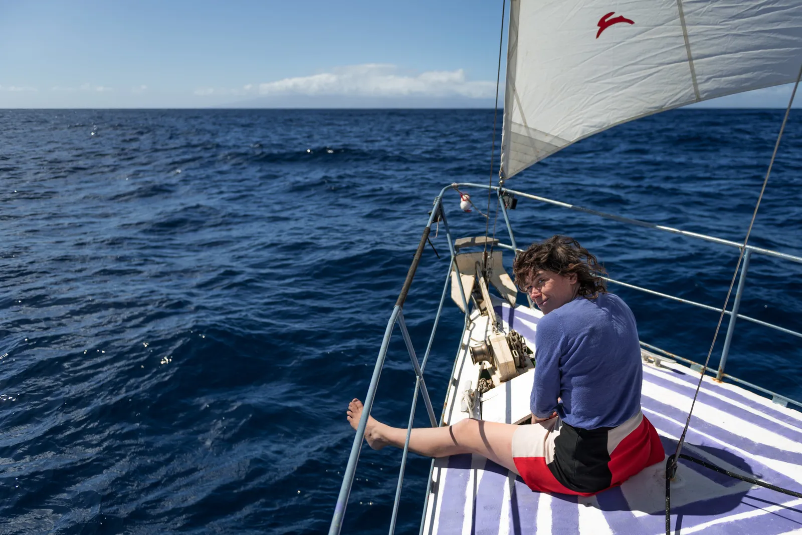 Person seated on the bow of a sailboat at sea