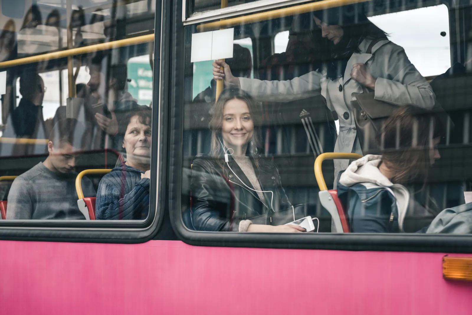 Passengers seen through a red bus window with city reflections