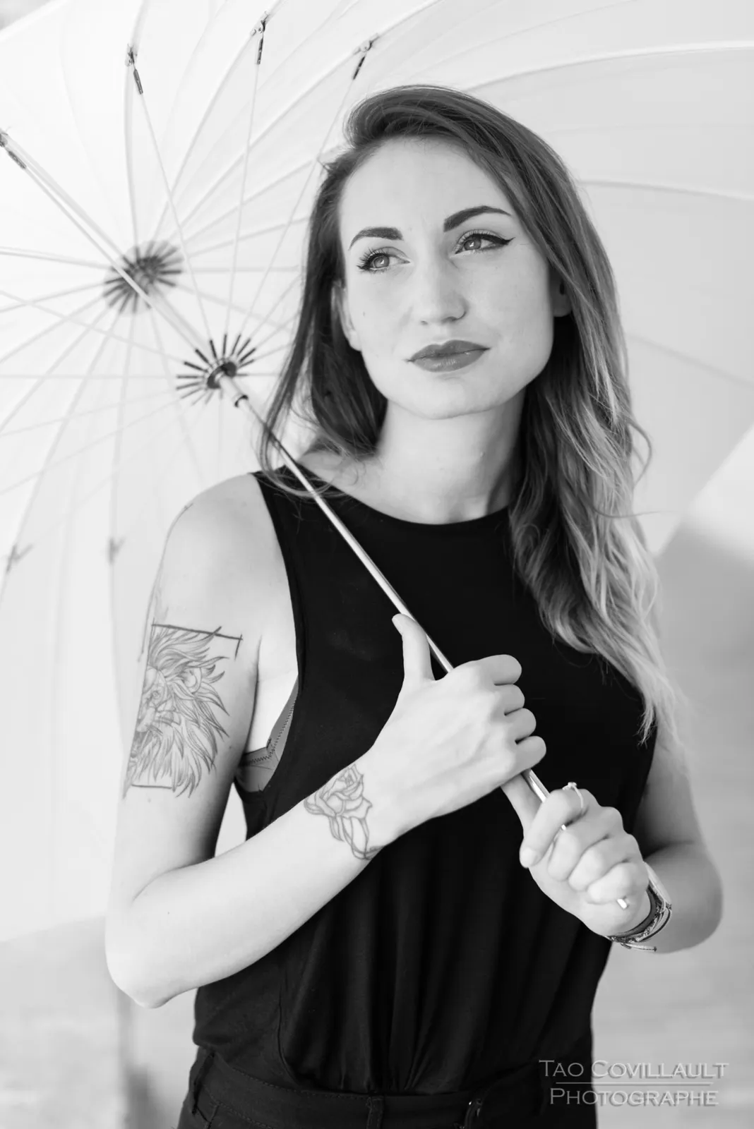 Black-and-white photograph: woman in black clothing holding a white parasol.