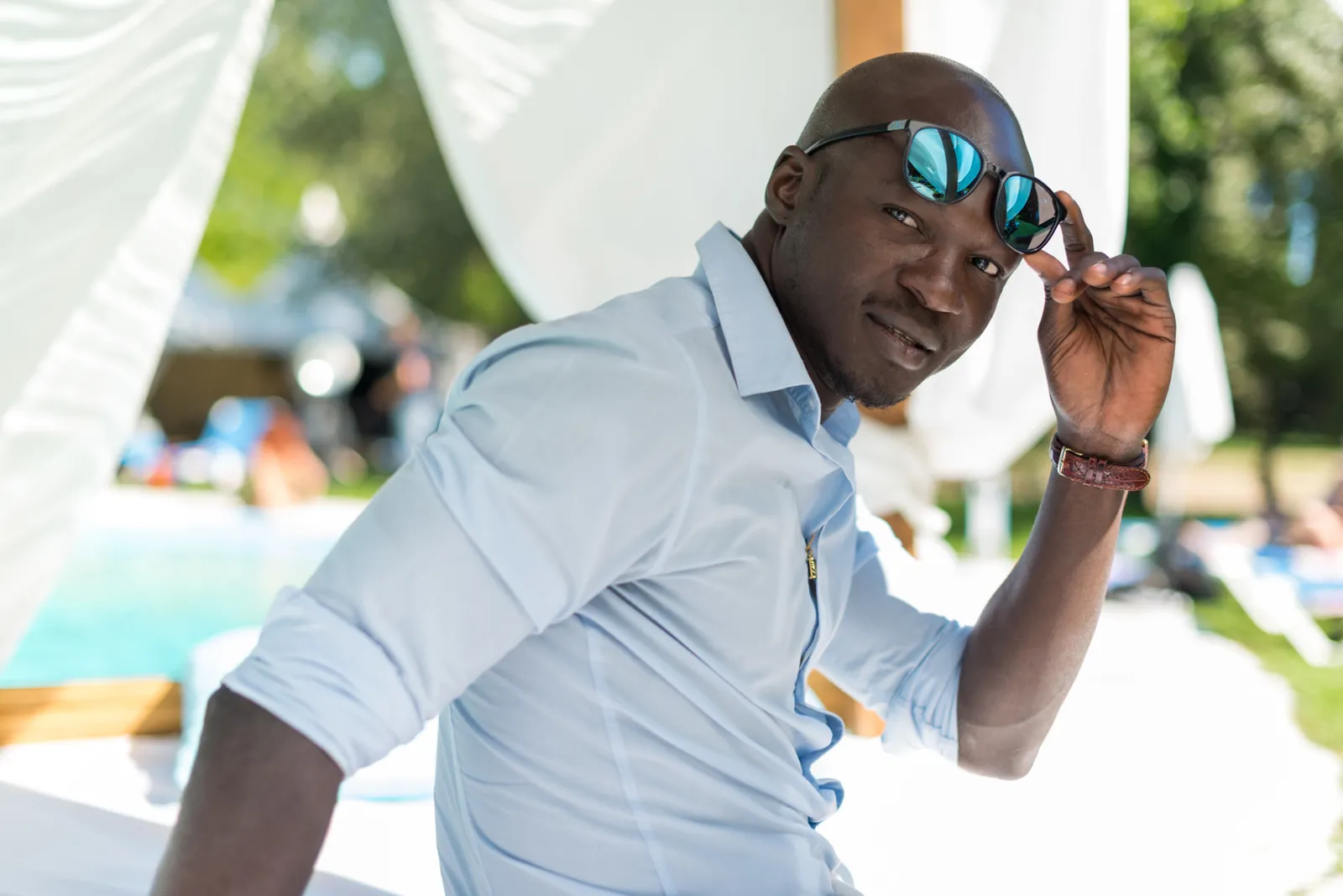 Man wearing sunglasses leaning beside a swimming pool.