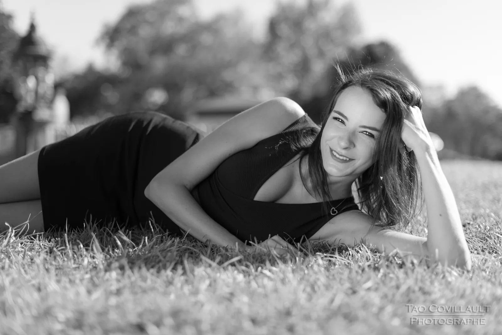 Black-and-white photograph: woman in a black dress relaxing on grass.