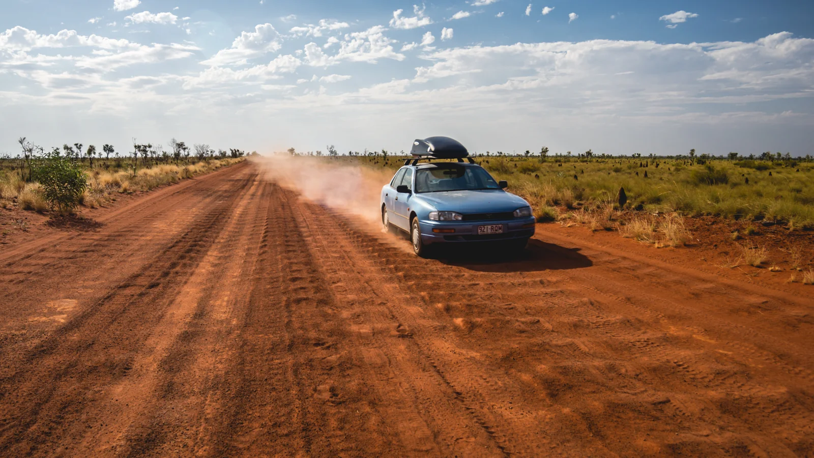 Blue car raising dust on a red dirt road